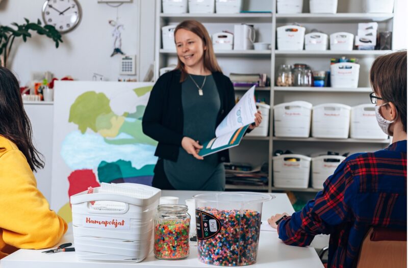 Seisova nainen puhuu kahdelle istuvalle nuorelle